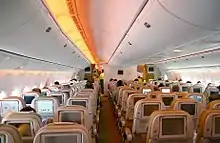 客機機艙。兩排座位排列在兩條走道之間。每個座椅靠背都有一個個人顯示器,其光線從側壁和頭頂行李箱照射進來。